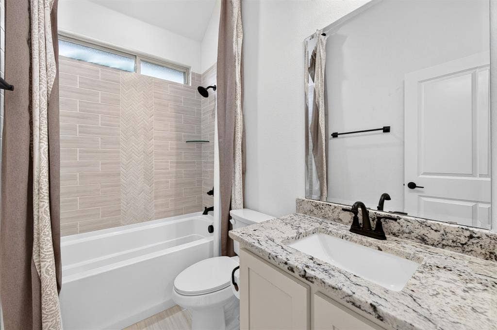 2600 Gavin Drive, Mansfield, TX 76063 Modern bathroom featuring a granite-topped vanity with an undermount sink and matte black faucet, framed mirror with black hardware, and a separate shower-tub combo with subway tile surround and glass enclosure