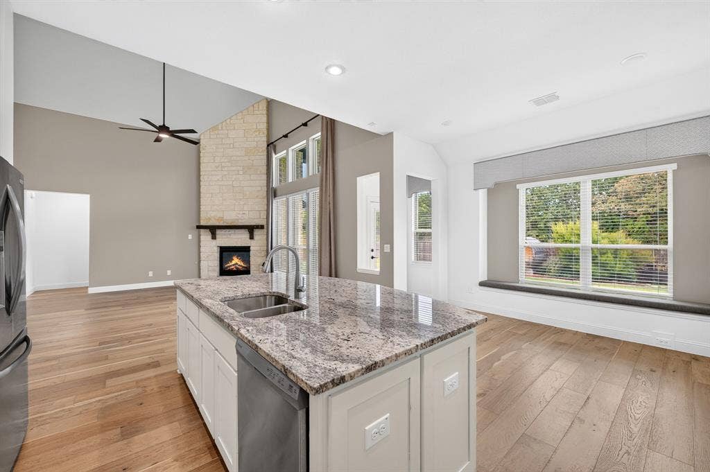 2600 Gavin Drive, Mansfield, TX 76063 Open-concept kitchen and living area featuring a large island with stone-finish countertops and stainless steel appliances, hardwood flooring throughout, recessed ceiling lighting, a ceiling fan, and expansive windows overlooking landscaped grounds