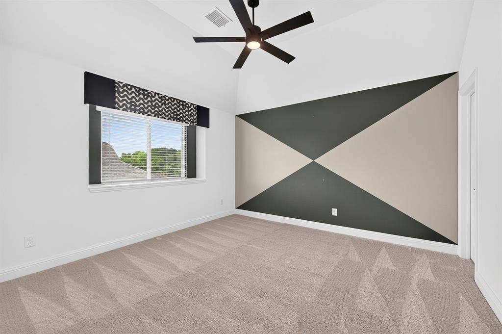2600 Gavin Drive, Mansfield, TX 76063 Modern bedroom #3 featuring plush wood-finish flooring, contemporary ceiling fan with dark metal blades, geometric accent wall with contrasting dark green and cream paneling, and abundant natural light from dual-pane window with integrated blinds and patterned valance