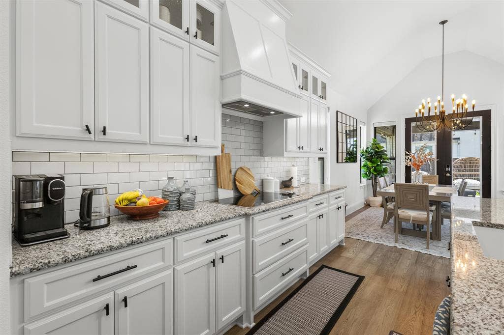 Kitchen featuring white shaker cabinetry, granite countertops, subway tile backsplash, and wood-finish flooring