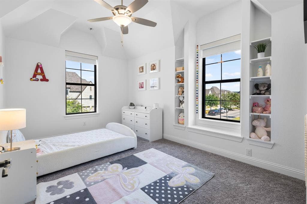 Vaulted ceiling, ceiling fan, white paneled walls, built-in shelving, and large windows