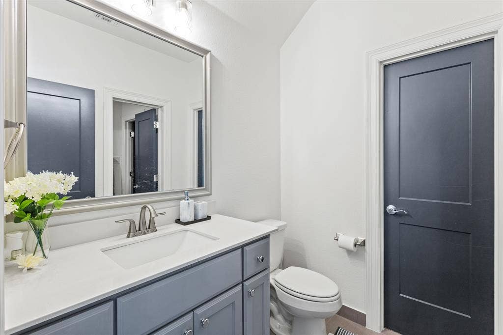 Single vanity with light gray cabinetry, white countertop, brushed nickel faucet, and a large framed mirror