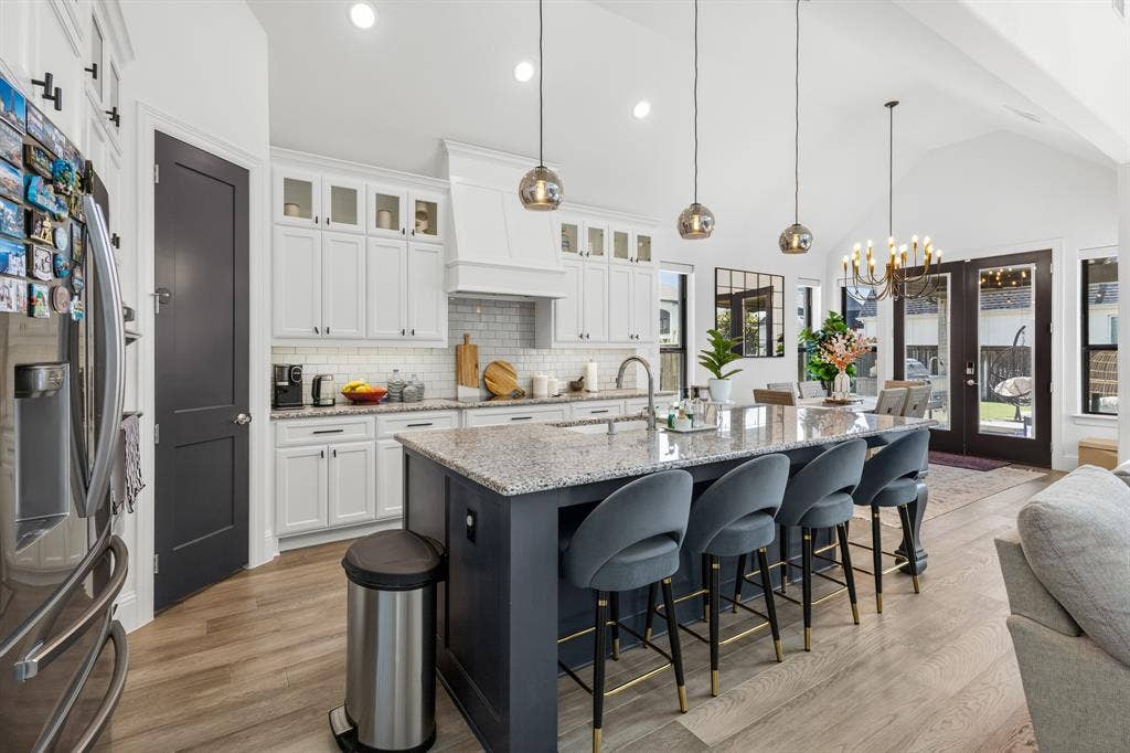 Spacious kitchen featuring an island with stone countertops, white shaker cabinetry, stainless steel appliances, and wood-finish flooring
