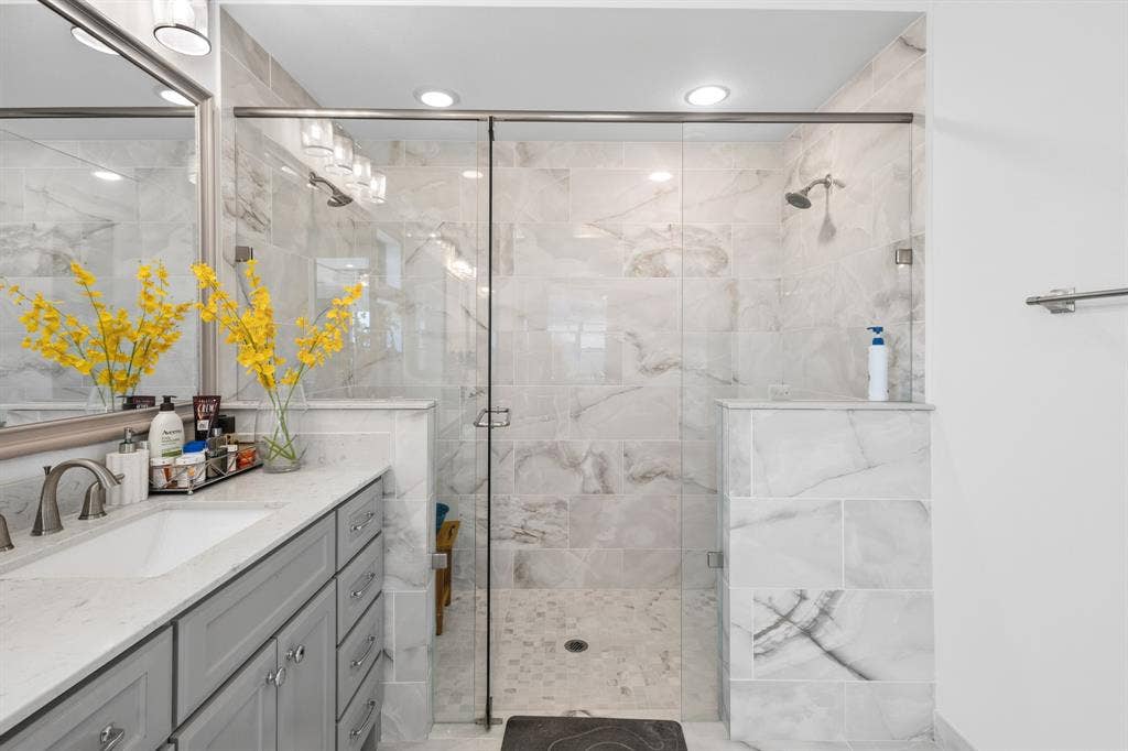 Glass-enclosed shower with dual shower heads, large format wall tile, and a built-in shower bench