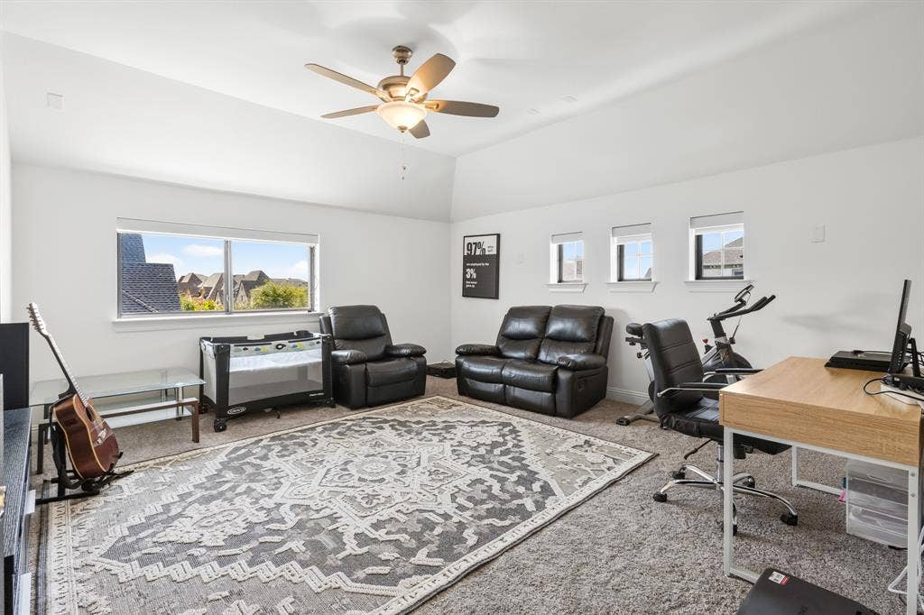 Spacious room featuring a vaulted ceiling with a ceiling fan, carpet flooring, a large window, and three smaller windows