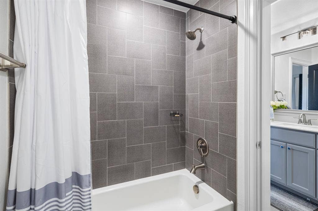 Subway tile shower surround with brushed nickel fixtures, white tub, and a vanity with a white countertop and blue cabinetry