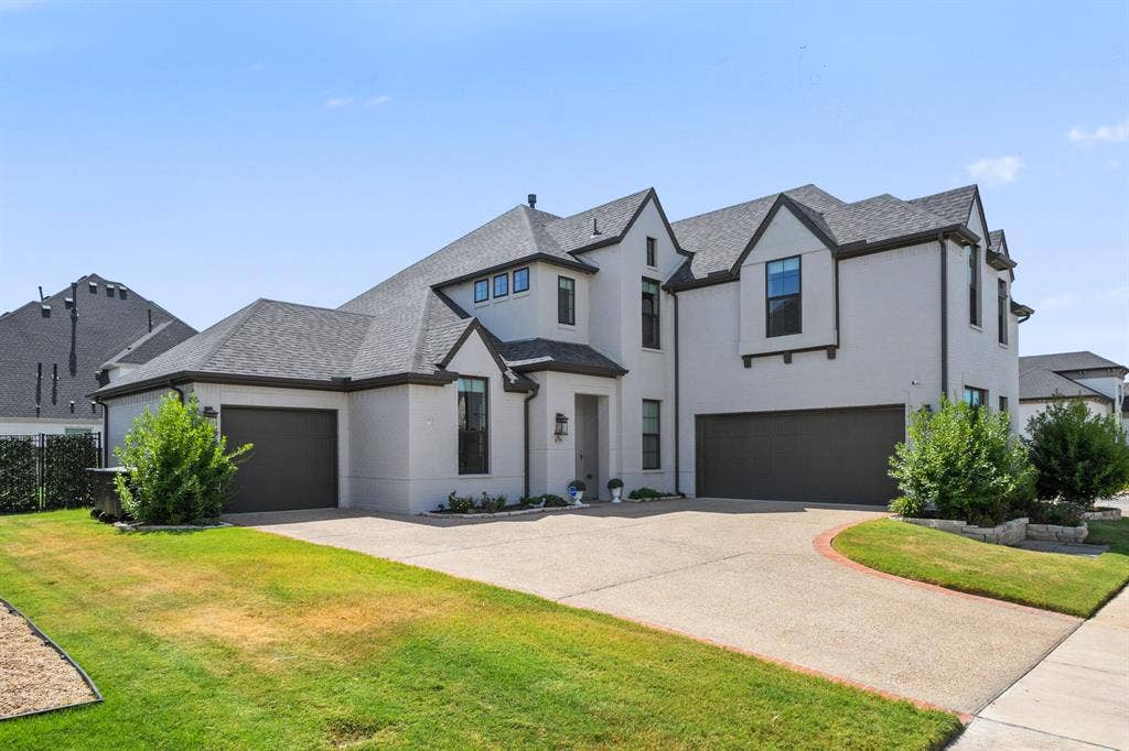 Stucco exterior with dark trim accents, multi-gabled roofline, multiple attached garages, and a concrete driveway