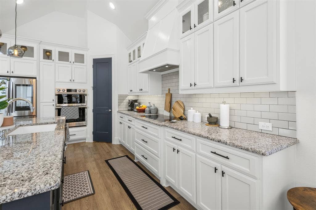 White cabinetry with dark hardware, granite countertops, subway tile backsplash, and wood-finish flooring