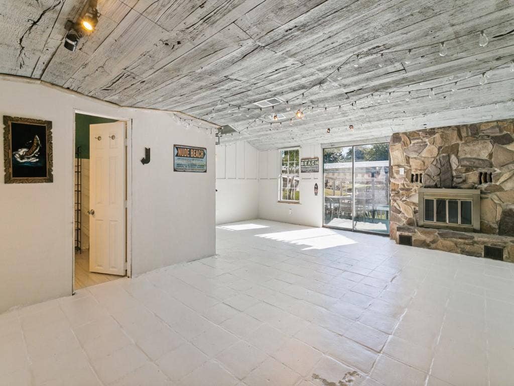 Stone-faced fireplace, distressed wood-finish ceiling, sliding glass doors, white tiled flooring, and recessed lighting
