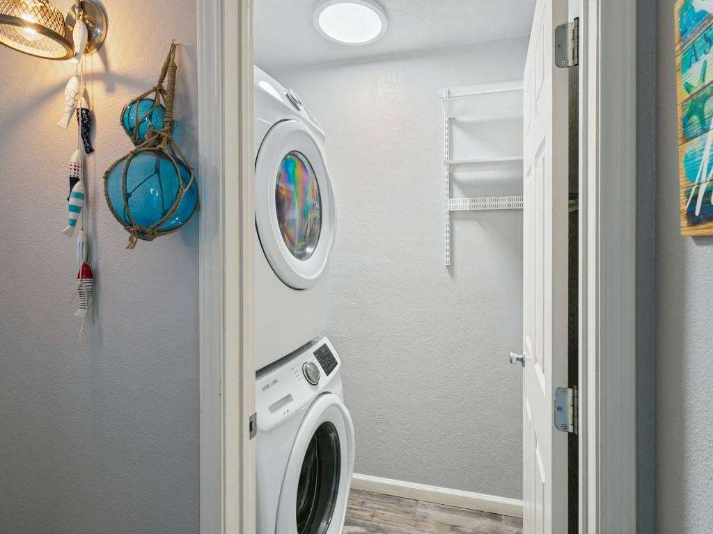 Stacked washer and dryer unit, wood-finish flooring, recessed lighting, and wall-mounted shelving