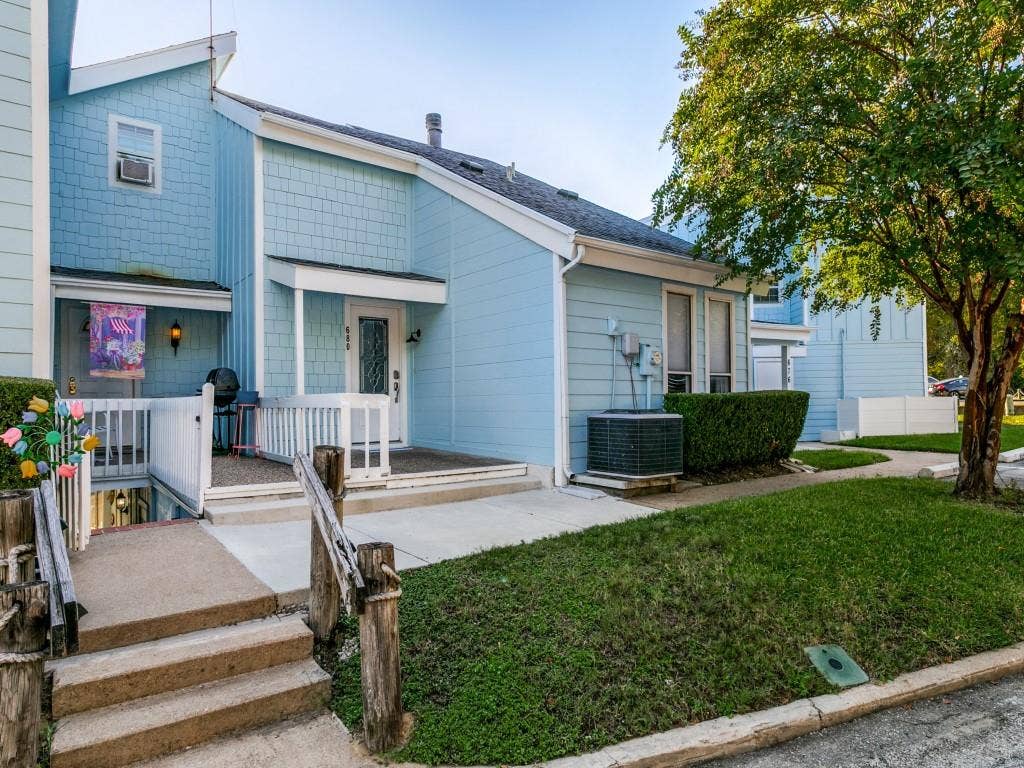 Light blue exterior siding with shake accents, a covered front porch, concrete entry steps, a manicured lawn, and mature trees