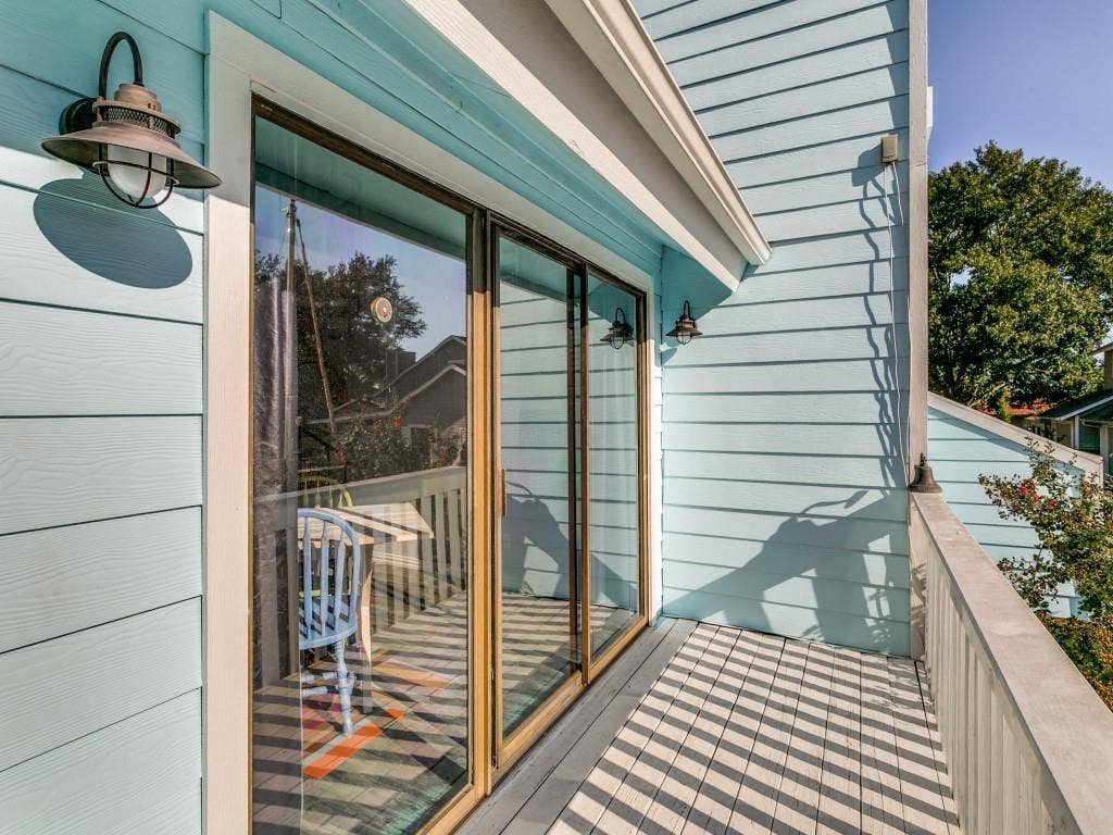 Upper-level balcony featuring a light blue exterior, sliding glass doors, built-in exterior lighting, and a durable railing