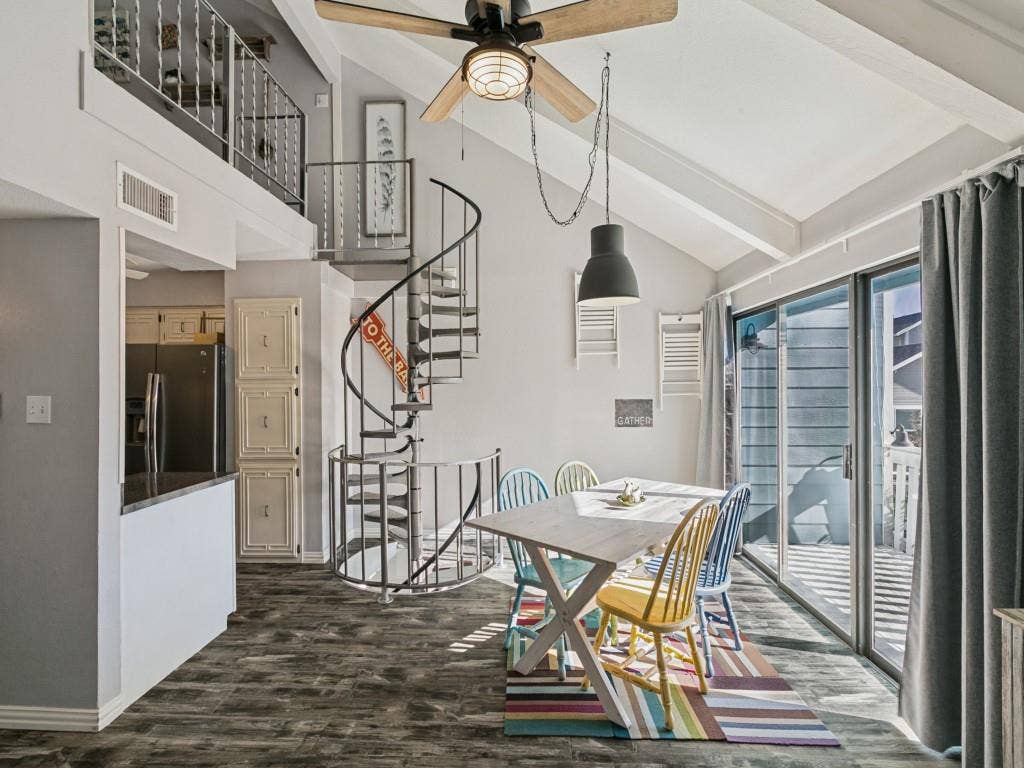 Vaulted ceiling with exposed beams, wood-finish flooring, sliding glass doors, spiral staircase, and an upper-level balcony