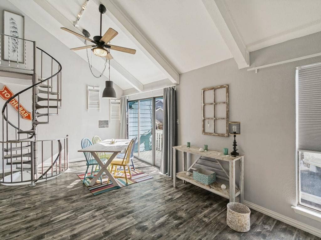 Vaulted ceiling with exposed beams, wood-finish flooring, black spiral staircase, and sliding glass door