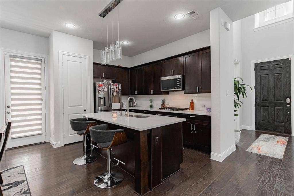 Kitchen island with a white countertop and seating, dark wood-finish cabinetry, stainless steel appliances, and wood-finish flooring
