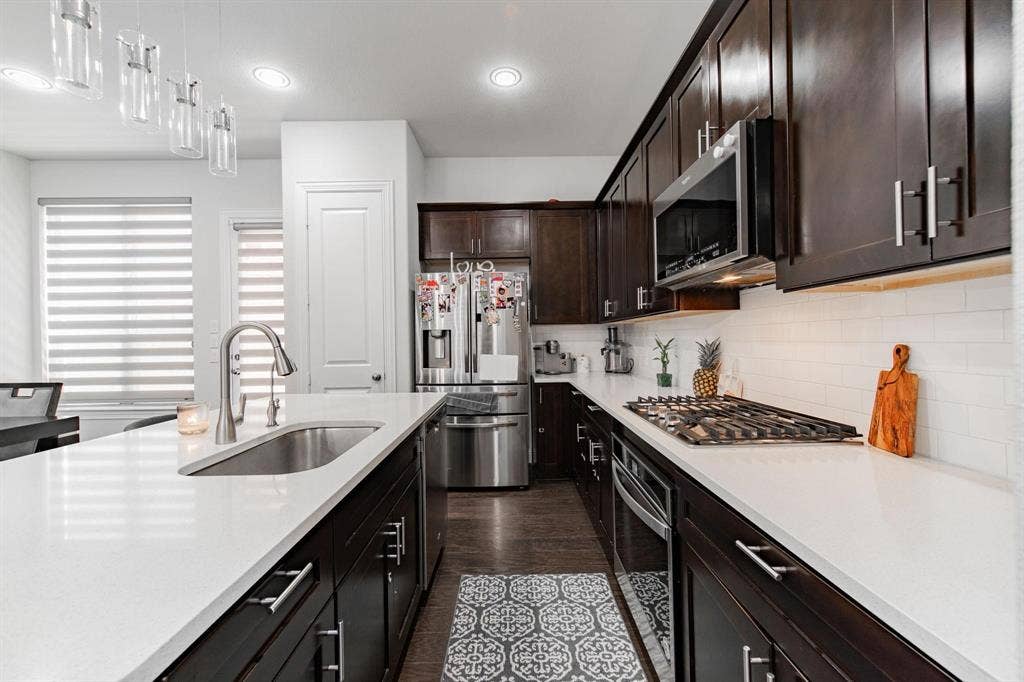 Contemporary kitchen featuring dark wood cabinetry, white countertops, stainless steel appliances, a gas cooktop, and a subway tile backsplash