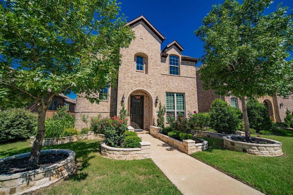 Brick exterior with arched entry, complementing landscaping, stone-clad planter beds, and a concrete pathway
