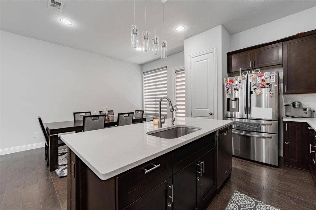 Kitchen island with a white countertop and undermount sink, dark wood-finish cabinetry, wood-finish flooring, and recessed lighting
