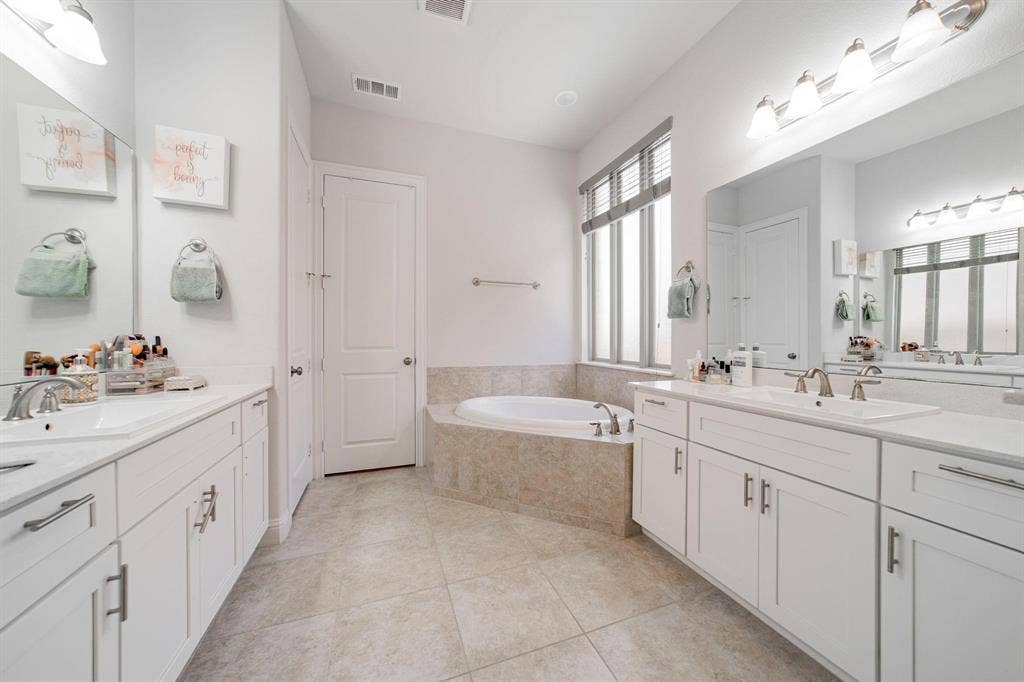 Spa-inspired primary bathroom featuring dual vanities with white cabinetry, marble-finish countertops, and polished chrome fixtures