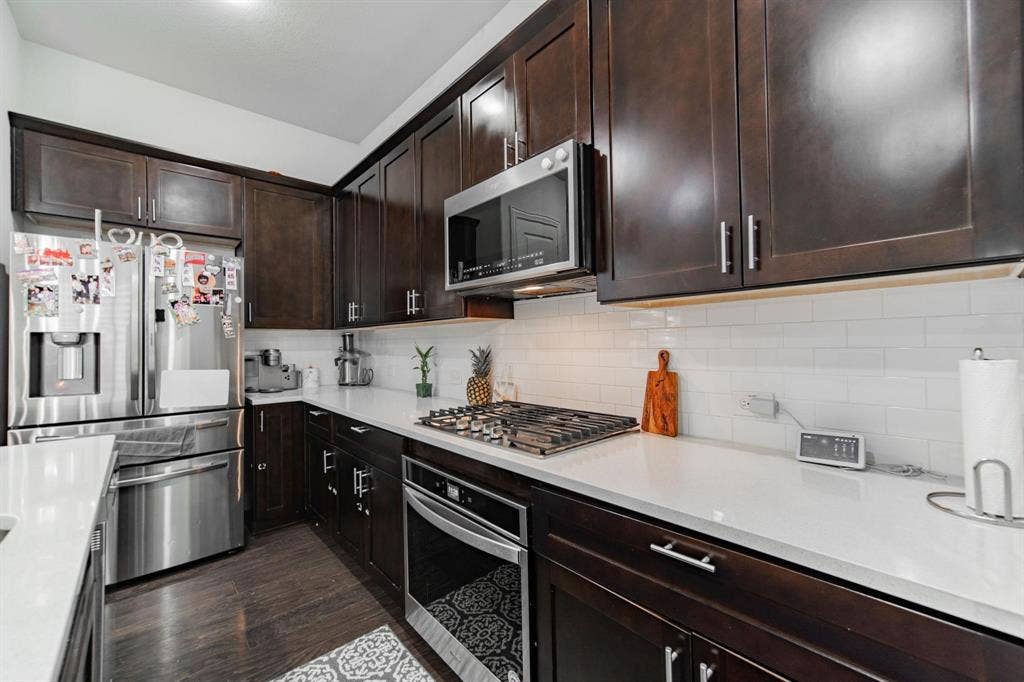 Dark wood-finish cabinetry, white countertop, subway tile backsplash, stainless steel appliances, and gas cooktop