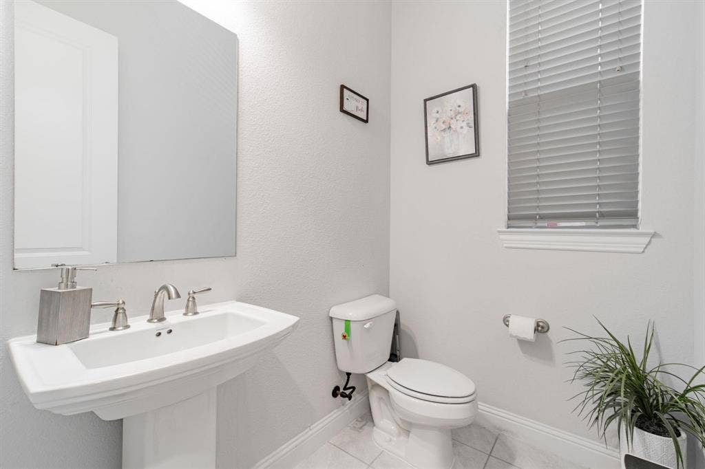 Pedestal sink with brushed nickel faucet, wall-mounted mirror, and a window with blinds