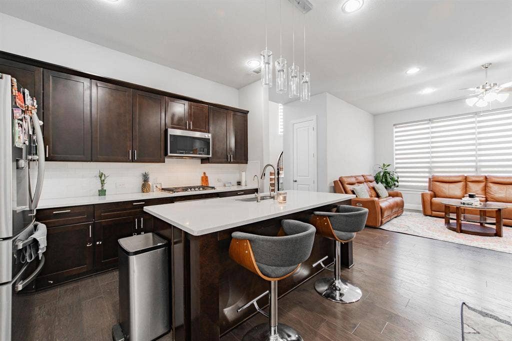 Kitchen island with white countertop, dark wood-finish cabinetry, stainless steel appliances, and wood-finish flooring