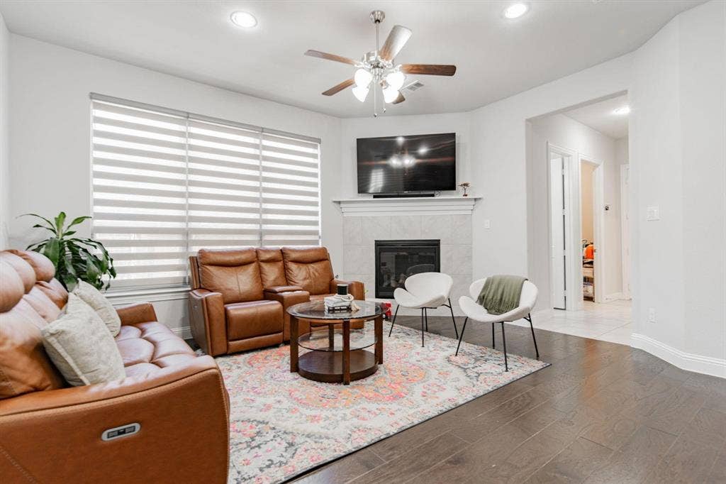 Spacious living area featuring wood-finish flooring, a ceiling fan, recessed lighting, and a fireplace with a mantel