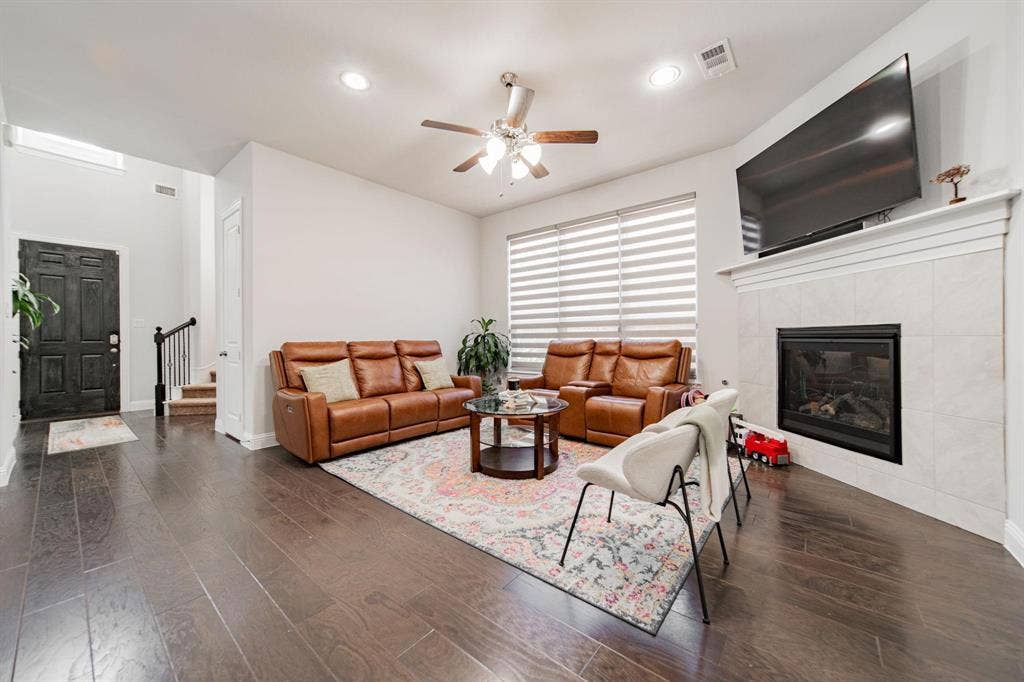 Spacious living area featuring dark wood-finish flooring, a ceiling fan with integrated lighting, recessed lighting, and a tile-surround fireplace with a mantel