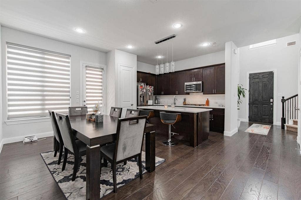 Wood-finish flooring throughout, kitchen with dark wood cabinetry, stainless steel appliances, a center island with countertop seating, and recessed lighting