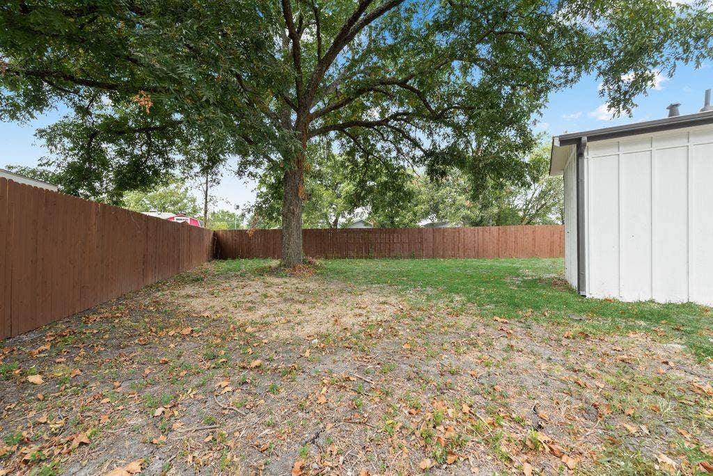 307 N 4th Street, Crandall, TX 75114 Expansive backyard featuring a mature shade tree, a wooden privacy fence, and a white exterior wall with vertical paneling