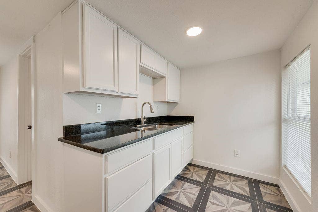 307 N 4th Street, Crandall, TX 75114 White cabinetry with dark countertops, stainless steel sink with gooseneck faucet, and patterned flooring