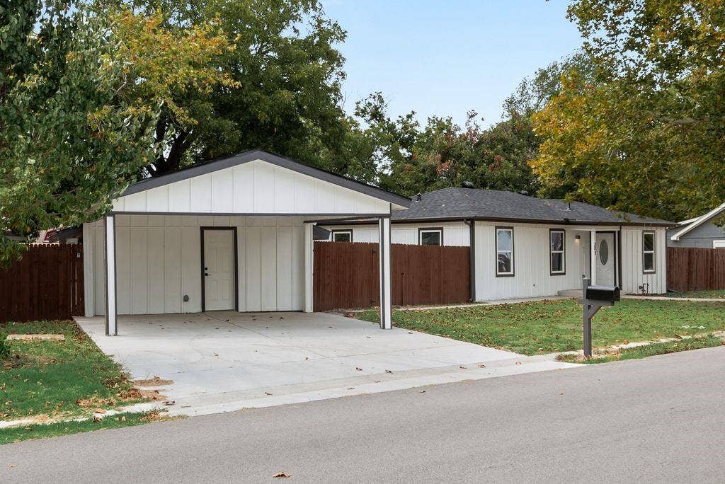 307 N 4th Street, Crandall, TX 75114 White siding exterior with dark trim accents, a covered carport, dark shingle roof, and a wood fence enclosing the property