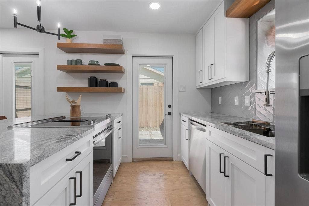 1805 W Spring Creek Parkway, #MM2, Plano, TX 75023 White cabinetry with black hardware, stone countertops, wood-finish open shelving, built-in stainless steel appliances, and a tile backsplash