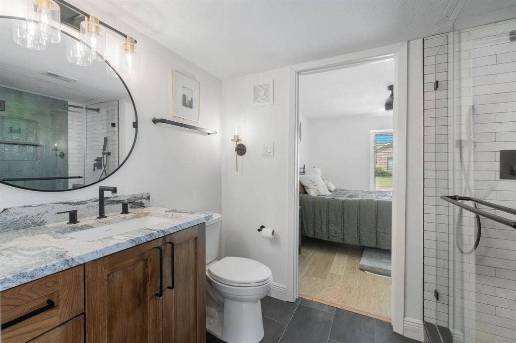 1805 W Spring Creek Parkway, #MM2, Plano, TX 75023 Bathroom featuring a wood-finish vanity with dual sinks, a large round mirror, and a walk-in shower with subway tile