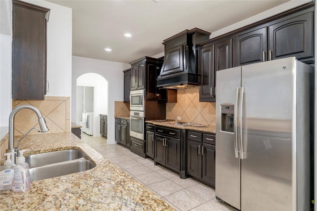 Kitchen featuring dark wood-finish cabinetry, granite-style countertops, stainless steel appliances, and a tiled backsplash