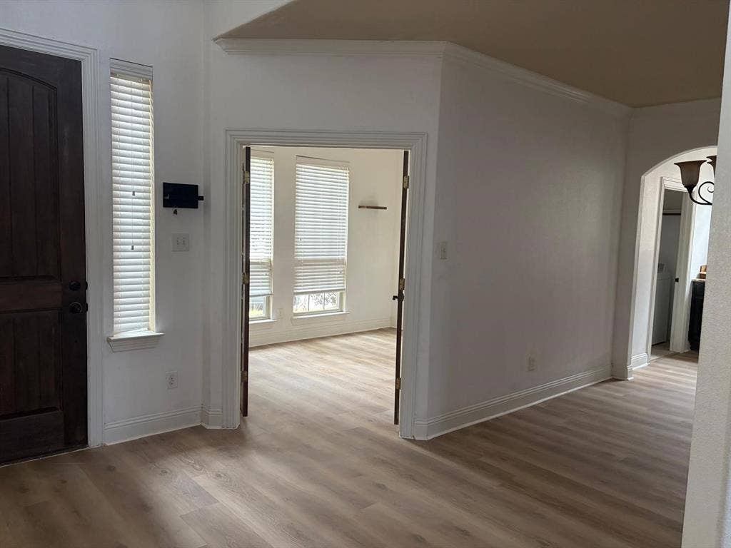 Wood-finish flooring throughout, arched entryway, crown molding, and bright windows with blinds