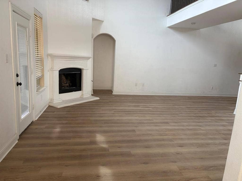 Vaulted ceiling, wood-finish flooring, white walls, arched doorway, and a fireplace with a white mantel and hearth