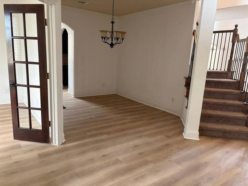Wood-finish flooring, dark wood French door with glass panels, arched entry, wrought iron staircase balusters, and a decorative chandelier