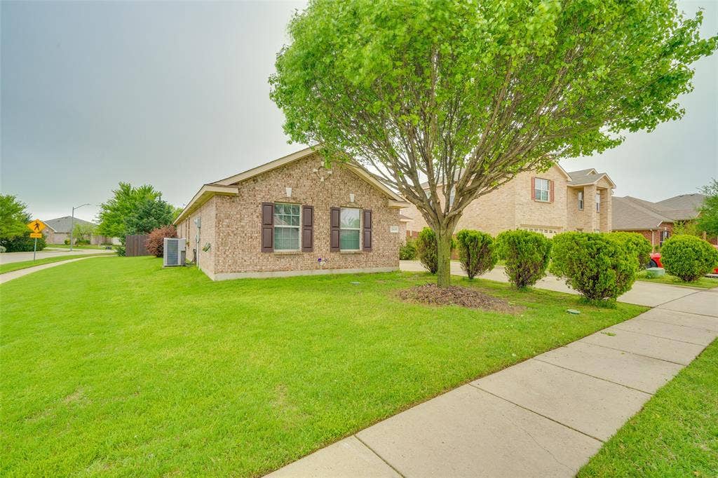 2035 Matagorda Lane, Grand Prairie, TX 75052 Brick exterior with brown shutters, mature shade tree, manicured shrubs, and a concrete sidewalk