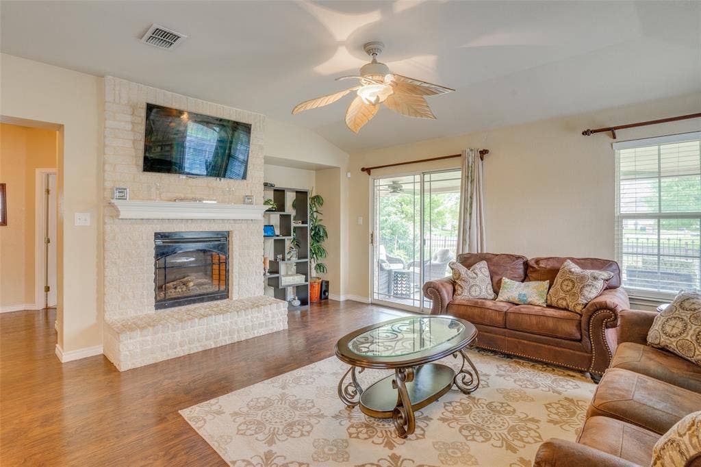 2035 Matagorda Lane, Grand Prairie, TX 75052 Living area featuring a stone-clad fireplace with a mantel, vaulted ceiling with a ceiling fan, and wood-finish flooring
