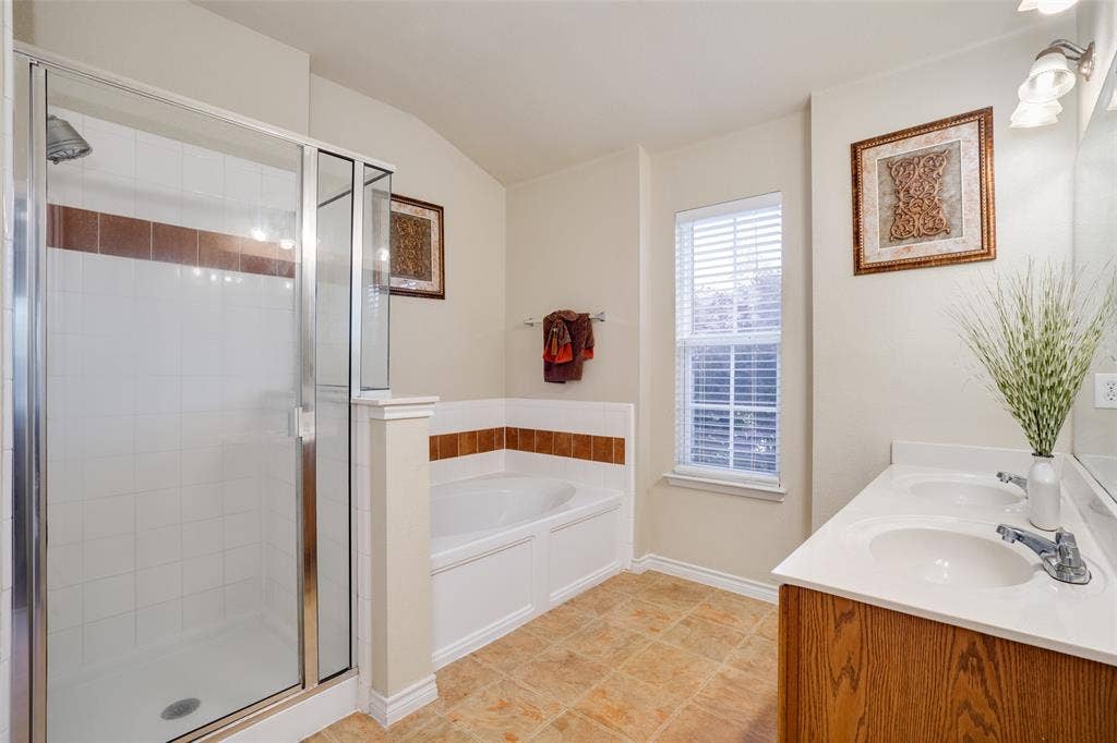 2035 Matagorda Lane, Grand Prairie, TX 75052 Tiled flooring with a white-tiled shower enclosure, a built-in bathtub, a window with blinds, and a double vanity with an integrated sink