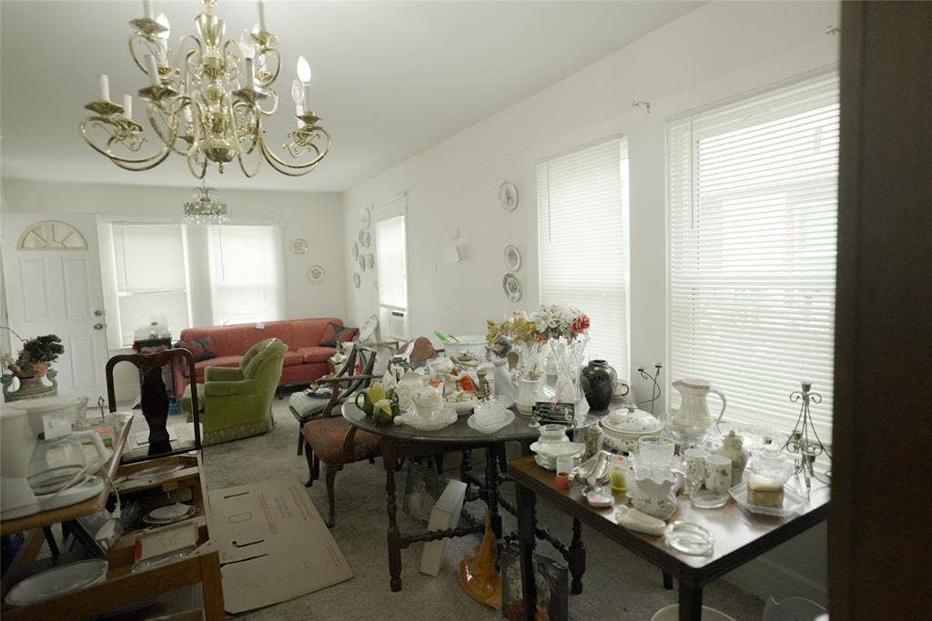 White walls with multiple windows featuring horizontal blinds, and a brass chandelier