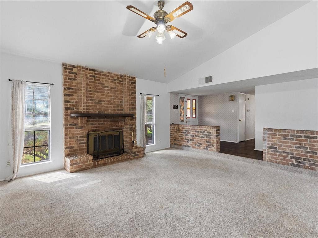 7612 Jerome Drive, Plano, TX 75025 Vaulted ceiling with a ceiling fan, brick fireplace with a wood mantel, light-colored carpeting, and a half-wall brick partition