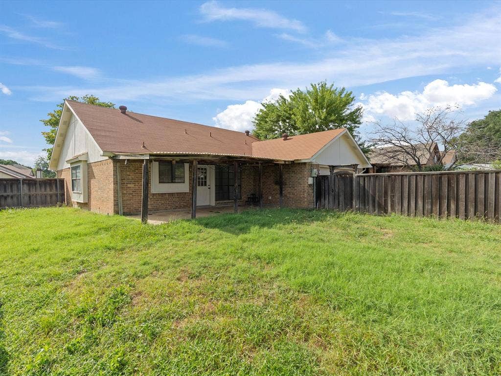 7612 Jerome Drive, Plano, TX 75025 Brick exterior with a covered patio, wood fencing, and a grassy yard