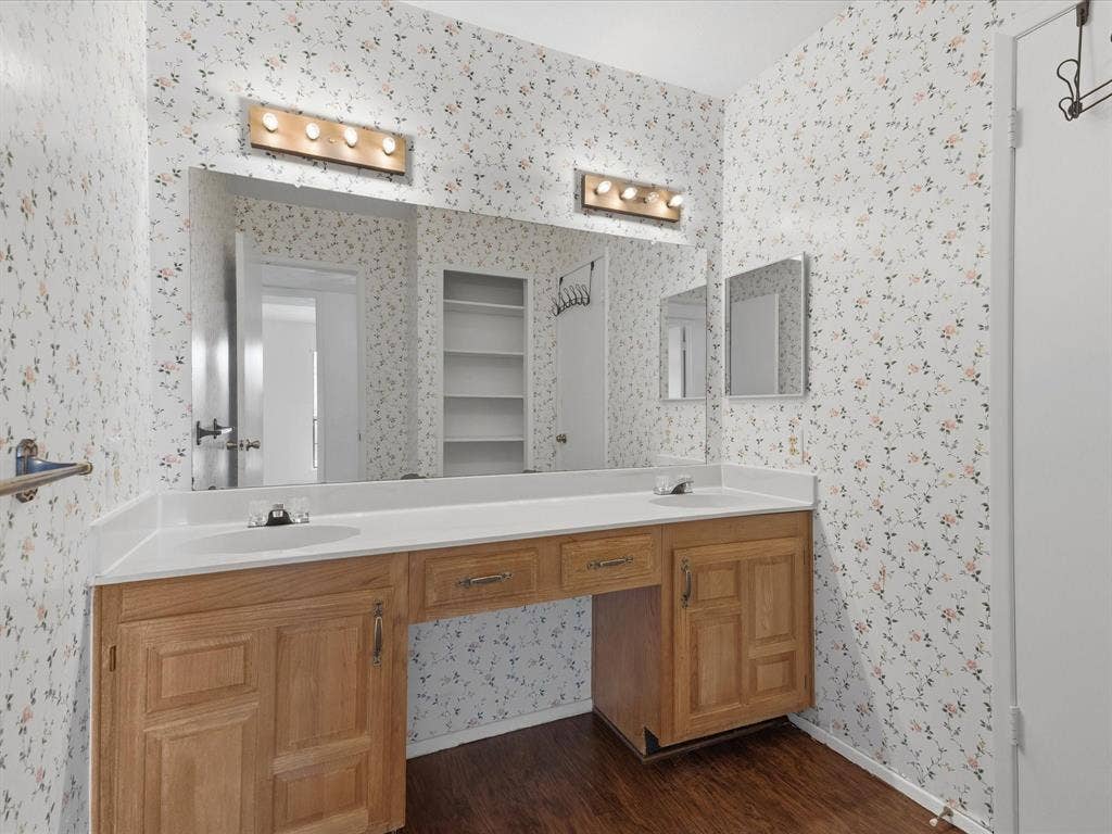 7612 Jerome Drive, Plano, TX 75025 Dual sink vanity with wood-finish cabinetry, integrated countertop, and laminate flooring