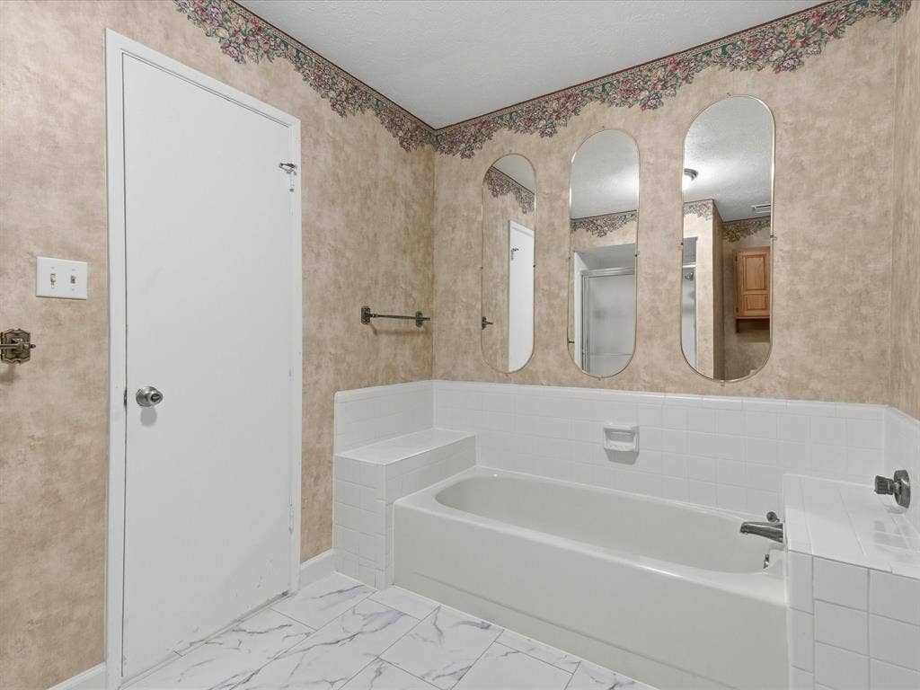7612 Jerome Drive, Plano, TX 75025 Bathtub with white tile surround, three wall-mounted arched mirrors, and white tile flooring