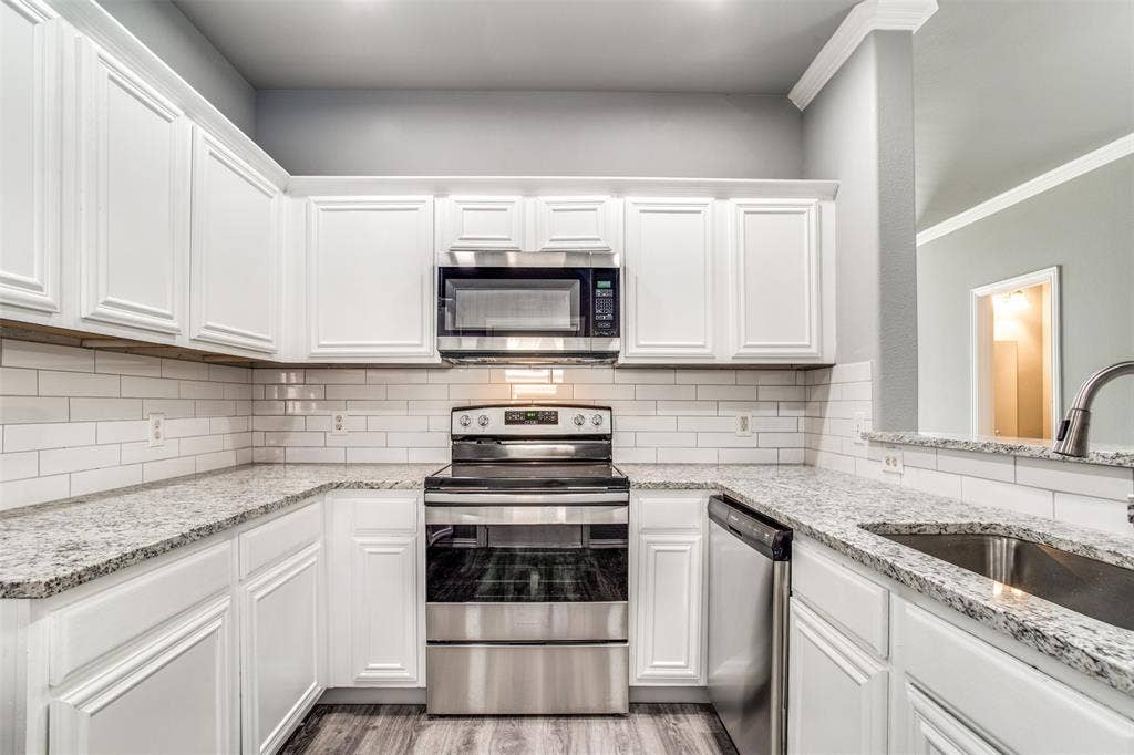 2364 Calendar Court, Grand Prairie, TX 75050 Kitchen featuring white shaker-style cabinetry, light-toned countertops, white subway tile backsplash, stainless steel appliances, and wood-finish flooring