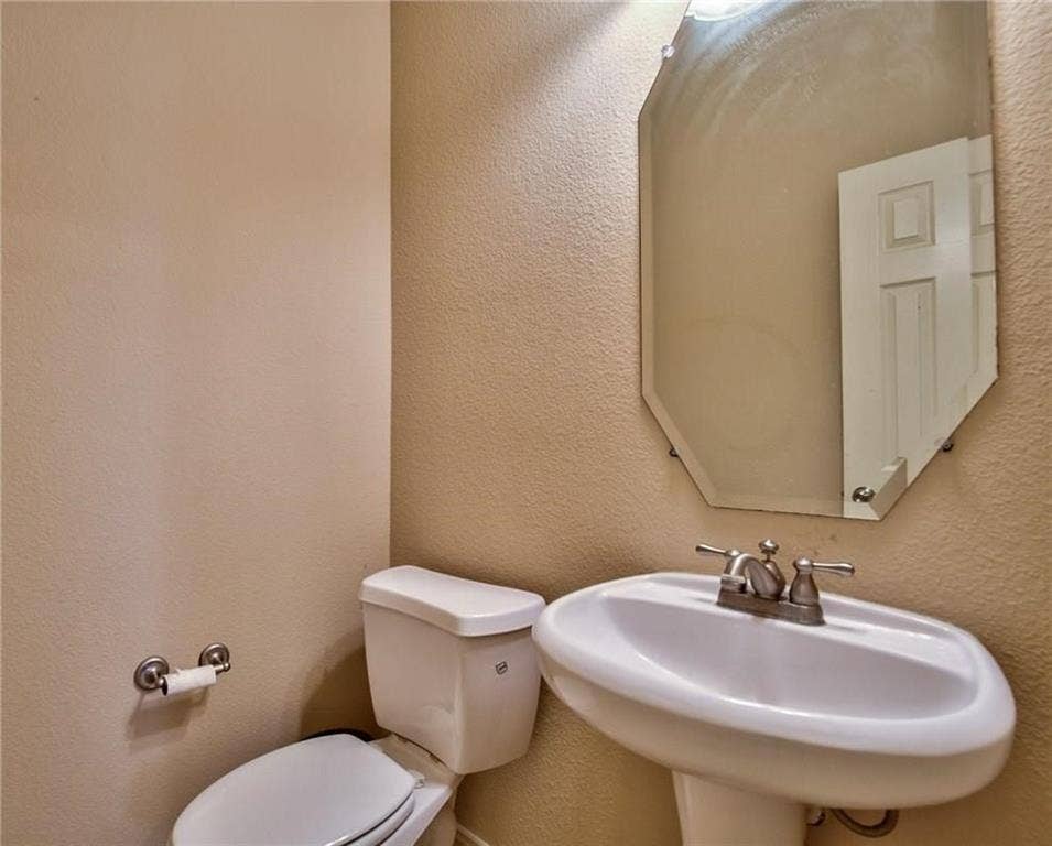 7108 Jessup Court, Plano, TX 75074 Pedestal sink, wall-mounted mirror with beveled edges, and a two-piece toilet