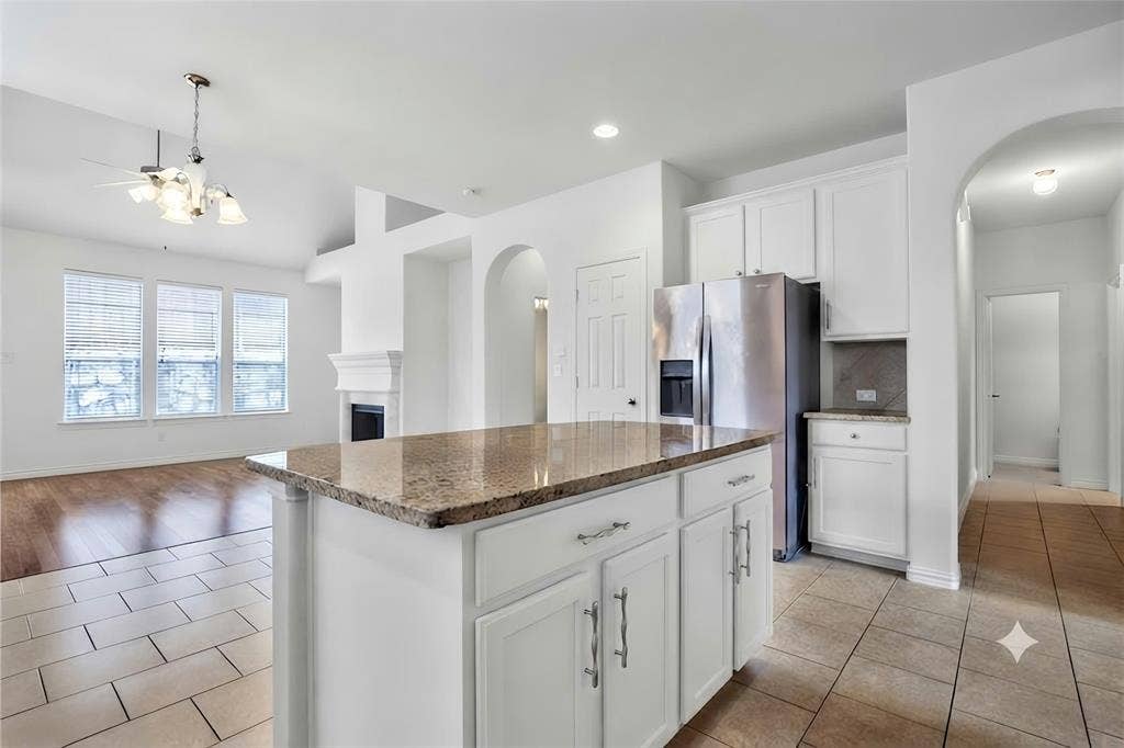 7108 Jessup Court, Plano, TX 75074 Kitchen island with granite countertop and white cabinetry, integrated stainless steel refrigerator, arched doorways, fireplace with mantel, and wood-finish flooring