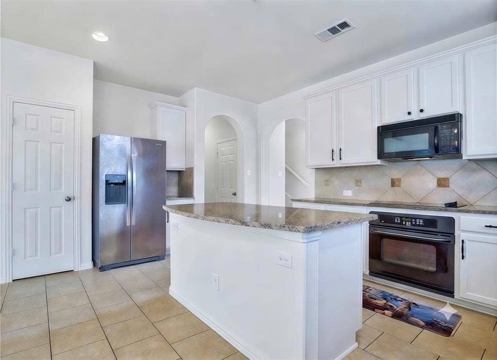 7108 Jessup Court, Plano, TX 75074 Kitchen featuring white cabinetry, a central island with a stone countertop, tile flooring, and a tile backsplash